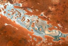 an aerial view of water and land in the middle of red earth with blue, white and brown colors