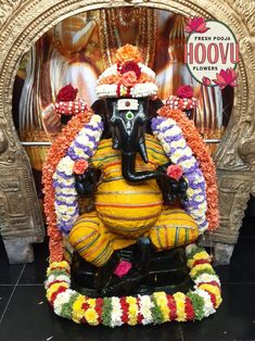 a statue of an elephant with flowers on it's head sitting in front of a gold frame