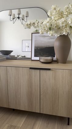 a vase filled with white flowers sitting on top of a wooden dresser next to a mirror