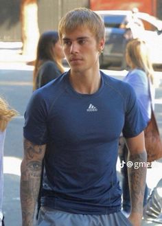 a man walking down the street with tattoos on his arm and shoulder, wearing a blue t - shirt