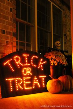 a lighted sign that says trick or treat next to pumpkins on the front porch