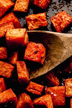 a wooden spoon full of cubed sweet potatoes on a black surface with brown flecks