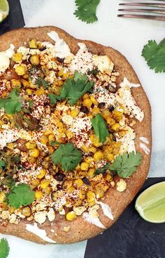 a pizza topped with corn, cheese and cilantro on top of a table