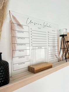 a wooden shelf topped with a black vase next to a dry plant and a white board