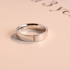 a white gold wedding ring with diamonds on it's side, sitting on top of a pink background