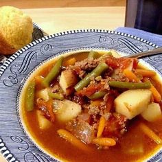 a blue and white plate topped with meat and vegetable soup next to a muffin