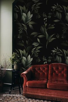 a red couch sitting in front of a black wall with green leaves and flowers on it