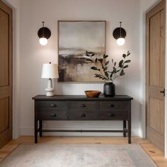 a table with two lamps and a painting on the wall above it in a hallway