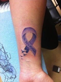 a woman's wrist with a purple ribbon tattoo on the left side of her arm