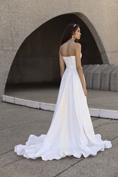 a woman in a white wedding dress is standing on the sidewalk with her back to the camera