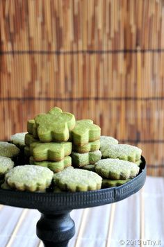 a black plate topped with green shortbreads on top of a wooden table next to a bamboo wall