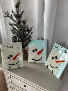 three snowmen painted on canvases next to a christmas tree