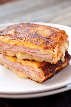 a ham and cheese grilled sandwich on a white plate with a wooden table in the background