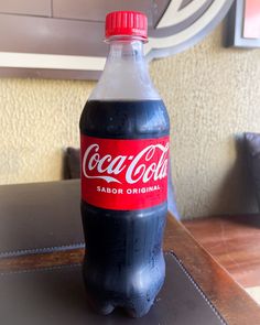 a bottle of coca - cola sitting on top of a table next to a wall