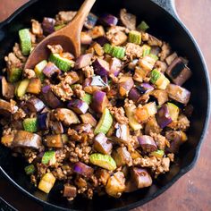 a skillet filled with meat and vegetables on top of a wooden table next to a spoon