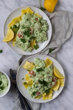 two plates filled with pasta and guacamole on top of a marble table