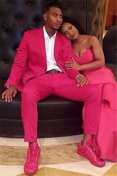 a man in a pink suit sitting next to a woman wearing bright pink shoes and a white shirt