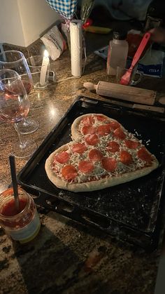 a pizza sitting on top of a pan covered in cheese and toppings next to wine glasses