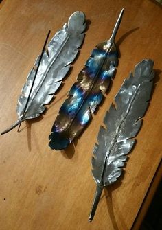 three metal feathers sitting on top of a wooden table