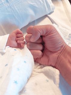 a person holding the hand of a baby who is laying on top of a bed