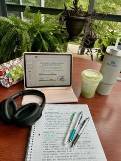 an open laptop computer sitting on top of a wooden desk next to headphones and pens