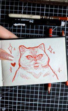 a drawing of a cat is being held up by someone's hand with some crayons on it