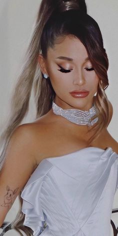 a woman with long hair wearing a white dress and diamond choker necklace, standing in front of a wall