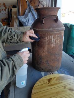 a man is painting a large vase on a table with a spray bottle next to it