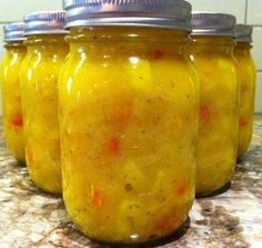 four jars filled with pickles sitting on top of a counter next to a tiled wall