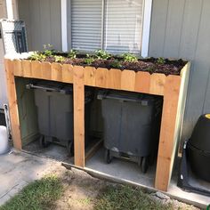 two trash cans sitting next to each other in front of a house with plants growing out of them