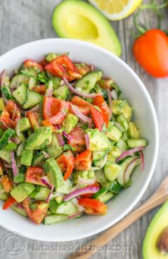 a white bowl filled with cucumber, tomato and onion salad on top of a wooden table