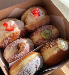 an open box filled with donuts covered in powdered sugar and fruit toppings