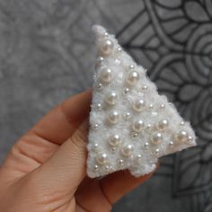 a hand holding a small white christmas tree brooch with pearls on it's side