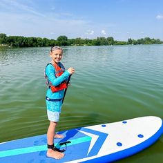 a woman standing on top of a blue and white surfboard next to a body of water