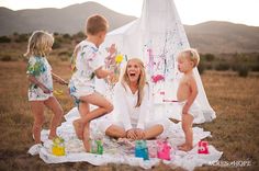 a woman sitting on top of a blanket next to two children in front of a teepee