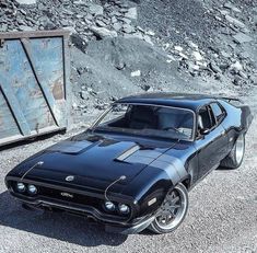 a black muscle car parked in front of a pile of rocks