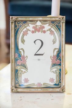 a white candle is sitting in front of a blue and gold frame with the number two on it