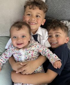 three young boys are sitting on a couch with their arms around each other and smiling at the camera