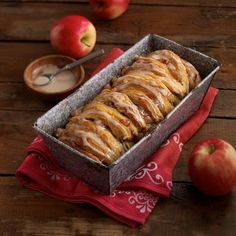 a loaf of cinnamon apple bread sitting on top of a wooden table next to apples