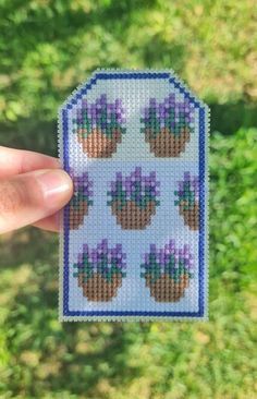 a hand holding up a cross stitch sticker with purple flowers on the top and bottom