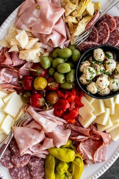 a white plate topped with different types of meat and cheeses next to olives