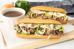 two sandwiches with meat, cheese and green peppers on a cutting board next to a cup of coffee