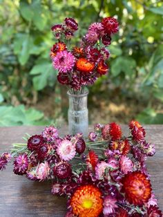 a vase filled with red and pink flowers on top of a wooden table next to greenery