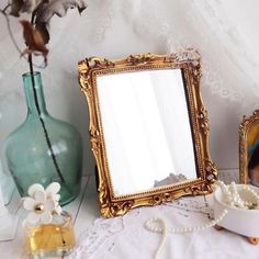 an ornate gold framed mirror sitting on top of a table next to a vase with flowers