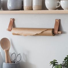 some cups and spoons are hanging on the wall next to a shelf with utensils