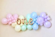 balloons spelling out the word one in gold and pastel colors on a white background