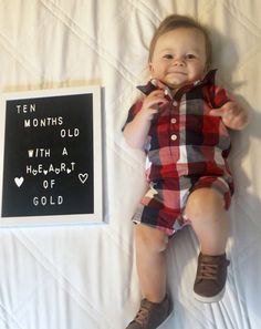 a baby laying on top of a bed next to a sign that says ten months old