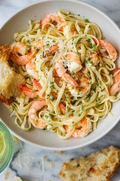 pasta with shrimp and parmesan cheese in a bowl next to garlic bread on a marble surface