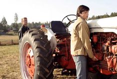 two young men standing next to an old farmall tractor in a field with other people looking on