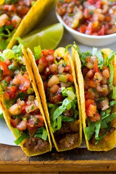 three tacos on a cutting board with salsa in the background